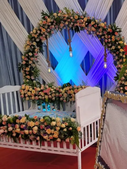 A side view showing the cradle and the circular floral arch against a backdrop of pleated white and blue drapes.