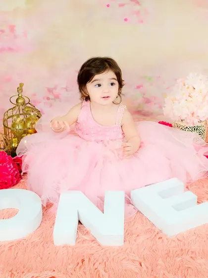 A princess-themed first birthday shoot with a baby girl in a pink tutu sitting among "ONE" blocks and floral decorations.