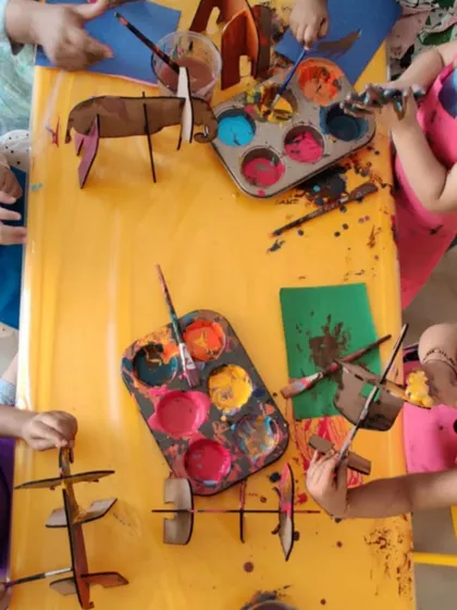 An overhead view of a busy art table during our elephant-themed workshop. You can see the colorful paint palettes and the unique cardboard elephant models each child is decorating.