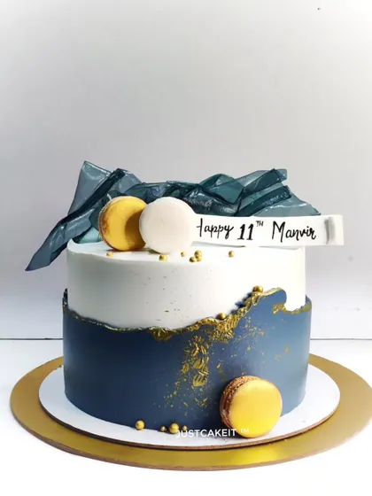 An abstract cake with a sophisticated navy blue and white color scheme. The design is accented with edible geometric sails and macarons.