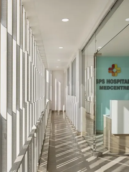 A detail of the corridor at SPS Hospital Clinic, showing the interplay of light and shadow created by the perforated facade. This design element adds a layer of visual texture and sophistication to the space.