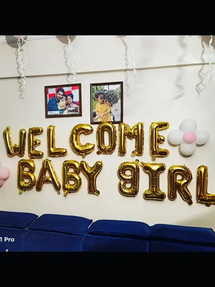 A 'Welcome Baby Girl' balloon decoration on a wall, complete with family photos, adding a personal touch to the celebration.