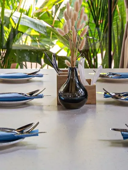 A close-up of a table setting at Vamos Experience. The crisp, striped chairs against the lush green background highlight the restaurant's indoor-outdoor feel, while the clean place settings suggest a high standard of service.