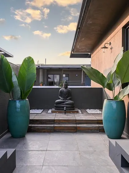 We transformed this outdoor space into a zen terrace with a wooden deck for a Buddha sculpture, concrete seating, and large teal urns, creating a perfect spot for entertaining or quiet contemplation.