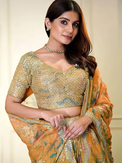 A pop of color for your celebration. This orange organza lehenga with a sequined blouse and floral skirt is designed for a fun and festive event like a Haldi or Sangeet.