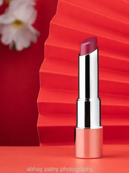A bold and elegant shot of a lipstick for a beauty brand. The red fan-shaped prop adds a touch of artistic flair and complements the product's color, creating a striking and memorable image.