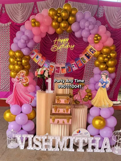 This Disney Princess theme is perfect for a first birthday. It features a pink, purple, and gold balloon arch, cutouts of Snow White and Sleeping Beauty, and stacked vintage-style suitcases for a fairytale look.