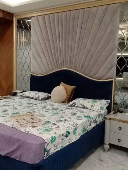 A close-up of a luxurious bed design. This features a dual-material headboard with a fan-shaped cushioned panel and elegant patterned mirror work on the sides, adding a touch of glamour.