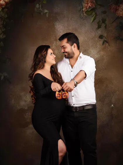 A classic couple's pose for an announcement. Holding up tiny baby shoes is a timeless way to share the happy news, captured here in a sophisticated studio setting.