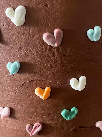 A tall chocolate cake that's as cute as it is delicious. The rich chocolate buttercream is covered in tiny, multi-colored piped hearts, making it a sweet and simple design for any birthday.
