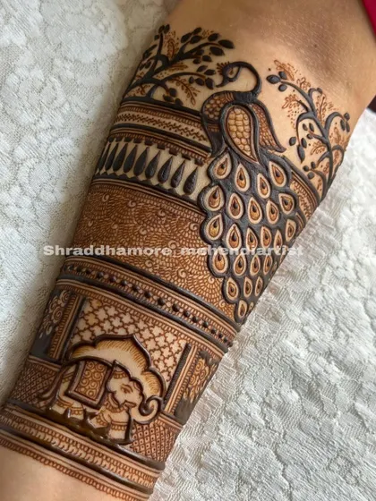 A classic bridal arm design starting with a majestic peacock surrounded by delicate branches. Below it, a decorated elephant adds a touch of royal procession to the artwork.