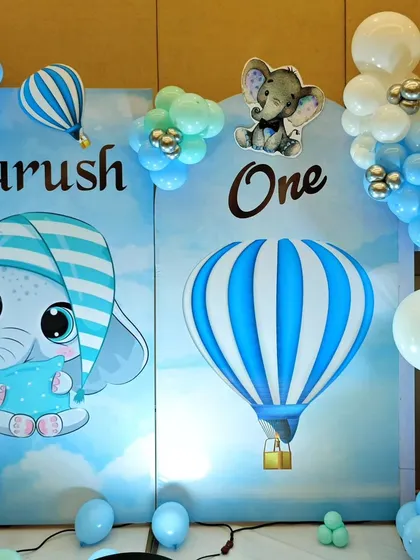 A sleepy baby elephant and hot air balloon theme for Aarush's first birthday. The backdrop creates a dreamy sky scene with clouds and stars.
