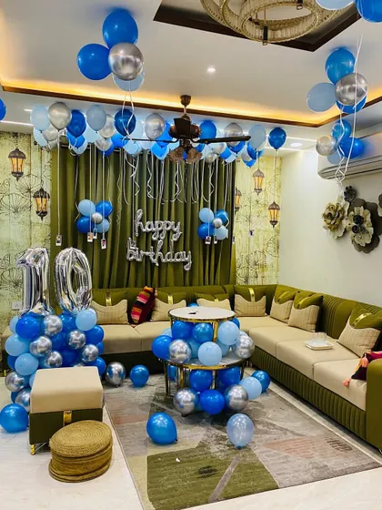 A 10th birthday decoration in a living room with a blue and silver theme. The setup includes balloon pillars for the number '10' and balloons on the ceiling.