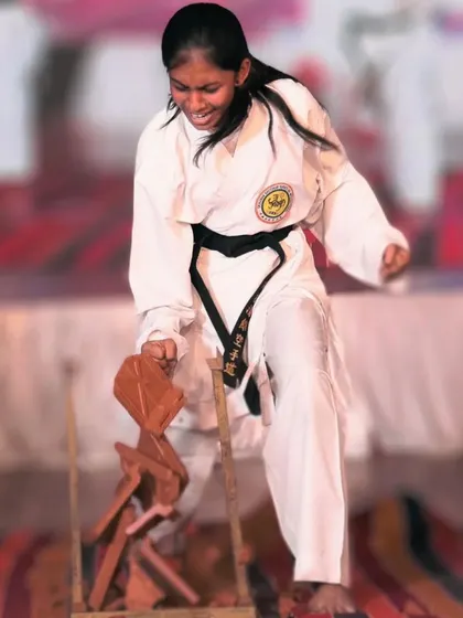 A young female student channels her full power into a downward strike, shattering wooden boards. This is a clear display of her focus and fighting spirit.