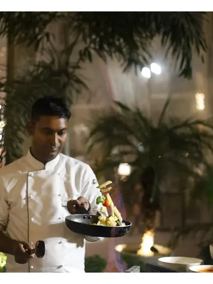 A chef artfully plates a freshly tossed pasta dish, adding height and garnish for a beautiful presentation straight from the live station.