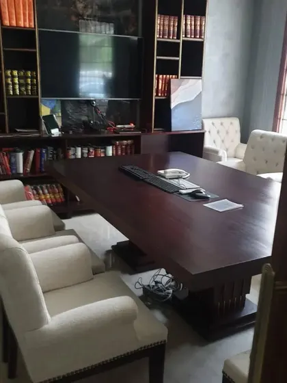 A home office setup featuring a large wooden table and classic upholstered chairs, set against a floor-to-ceiling bookshelf. It's a perfect blend of a library and a workspace.
