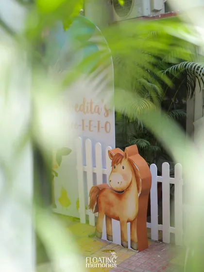 A glimpse of the party entrance through the lush greenery. A friendly horse cutout and a white picket fence welcome guests to Nivedita's 'Three-i-e-o' celebration.