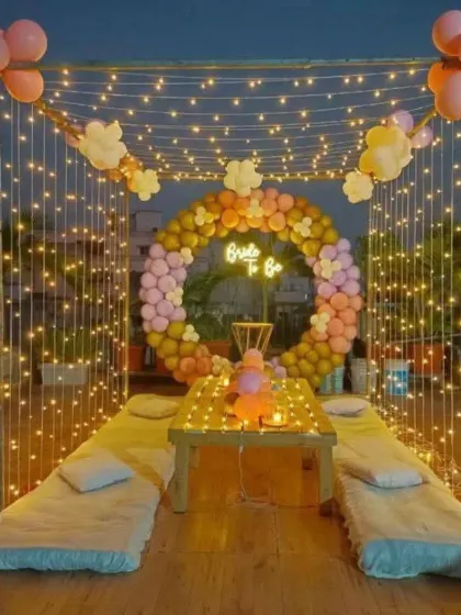 We transform any space into a magical setting. This intimate rooftop setup for a 'Bride-to-be' party features a canopy of fairy lights, low seating for a cozy vibe, and a neon sign, perfect for a memorable evening under the stars.