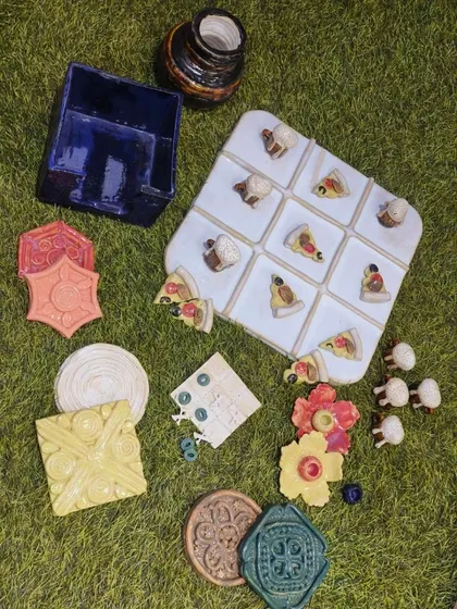 An assortment of exquisite ceramic pieces created by one of our students, Sejal. This collection includes decorative tiles, flower-shaped candle holders, and a playful tic-tac-toe set.