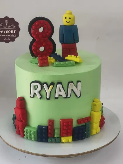 A Lego-themed cake for an 8th birthday, featuring a handcrafted Lego man and colorful blocks. The light green frosting provides a great backdrop for the primary-colored decorations.