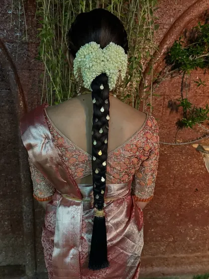 A classic South Indian bridal hairstyle featuring a heart-shaped jasmine arrangement. The braid is decorated with delicate gold teardrop accessories for a simple and elegant look.