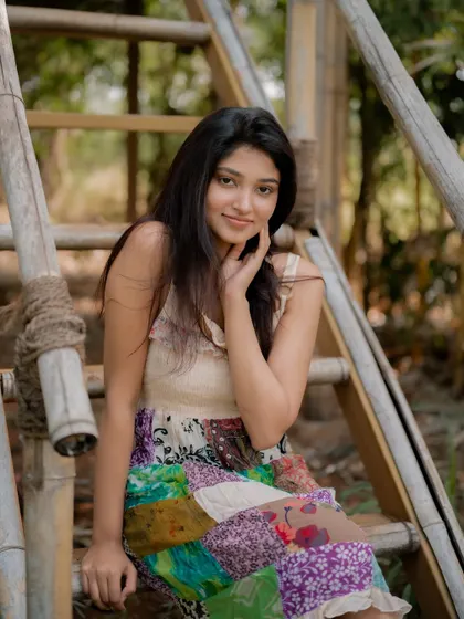A candid and happy portrait of actress Rachana Inder on a bamboo ladder. The natural, outdoor setting and her bright smile create a joyful and authentic image.