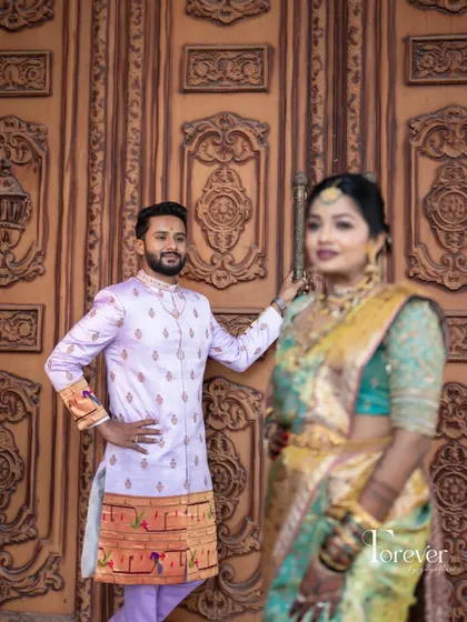 In this photo, you can see how the groom's custom Paitani silk sherwani in lavender stands beside his bride. The traditional weave and color of his outfit create a lovely contrast that enhances both their looks.