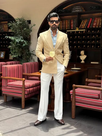 We believe a suit should be an extension of your personality. This bespoke double-breasted jacket in a refined beige, paired with crisp white trousers, is crafted for sophisticated day events and elegant soirées. It showcases a powerful silhouette and impeccable tailoring.