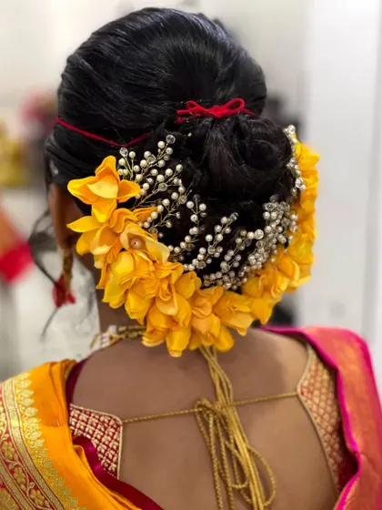 A close-up of a traditional bridal bun for a Maharashtrian wedding. The bun is beautifully decorated with yellow flowers and a pearl-studded 'gajra' accessory.