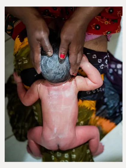A powerful top-down photograph of a newborn receiving a traditional massage. The vibrant colors of the cloth contrast beautifully with the baby's delicate skin.
