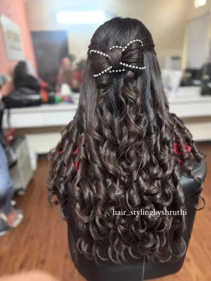 A fun and youthful half-up style with tight curls and a large, pearl-studded hair bow. This is a statement look that is perfect for a party or a pre-wedding celebration.