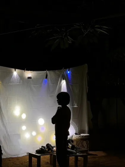 A child stands in silhouette against the brightly lit moth screen, waiting in quiet anticipation for the nocturnal visitors to arrive.