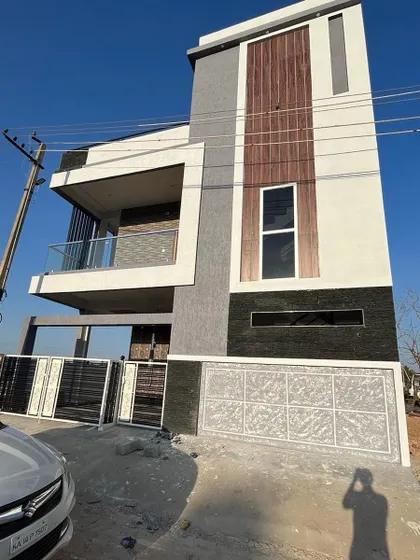 A completed home in Shimoga, ready for handover. The design features a mix of textures, including wood-look panels and stone cladding, with a glass balcony that adds a modern touch.