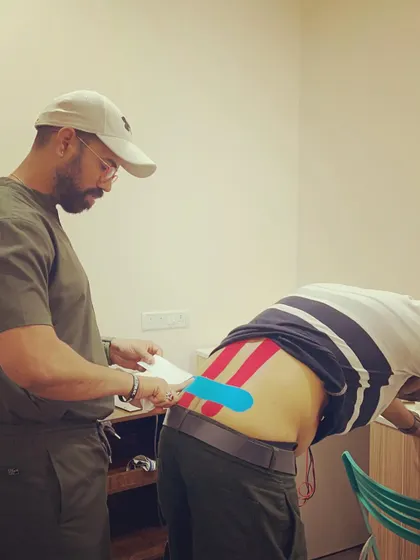 The process of applying different colored kinesio tapes to a client's lower back. The specific pattern and tension are designed to offload strained muscles and facilitate better movement.