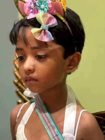 A child dressed as a unicorn angel, with a colorful headband and a thoughtful expression, taking in the party atmosphere.