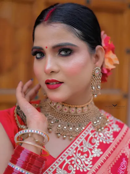 A tight close-up focusing on the woman's face. The shot highlights her bold red lip, traditional bindi, and elegant gold jewellery.