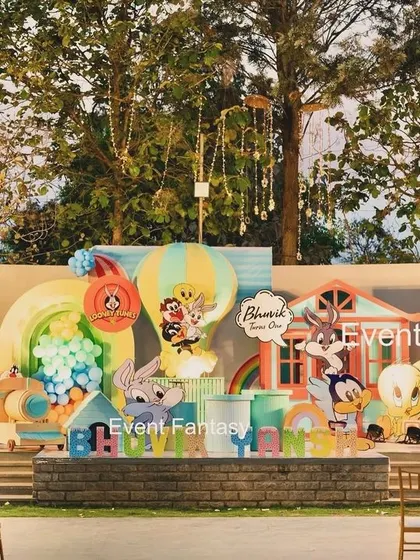 That's all, folks! A grand Looney Tunes first birthday celebration for Bhuvik. This expansive outdoor stage brings the classic cartoon to life with large cutouts of Bugs Bunny, Sylvester, Daffy Duck, and the whole gang, complete with colorful balloon art and themed houses.