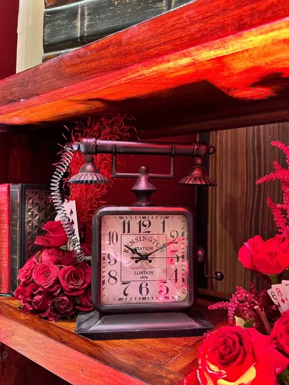 A vintage telephone-clock adds a touch of nostalgia and charm to a shelf display, surrounded by red roses and old books.