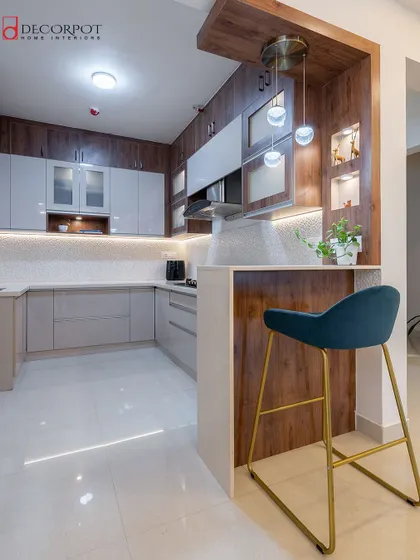 This U-shaped kitchen features a breakfast bar with a stylish teal stool, creating a functional link between the kitchen and the rest of the living space. The wood and grey tones give it a warm, contemporary feel.