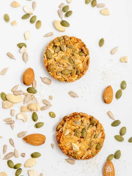 An artistic shot of our multi-seed cookies, surrounded by the raw ingredients we use. You can see the quality of the almonds, cashews, and various seeds that go into every batch.