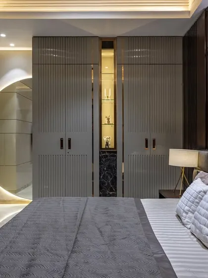 This modern bedroom uses a monochromatic gray palette with clean lines and geometric textures. A backlit circular mirror creates a striking visual element and breaks the linearity of the fluted wardrobes.