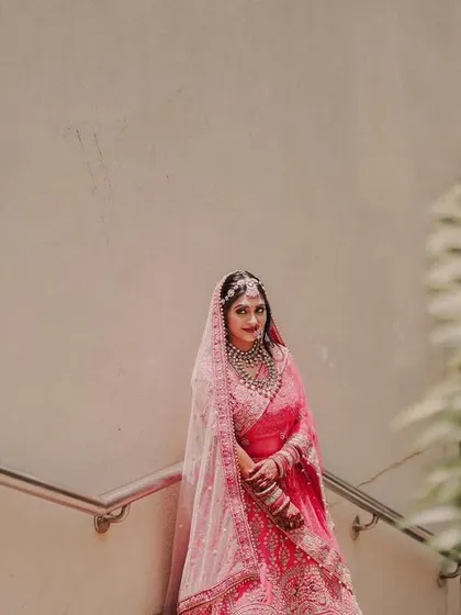 A wide shot of the bride on a staircase, framed by a large plant. This composition gives a sense of scale and elegance to her bridal portrait.