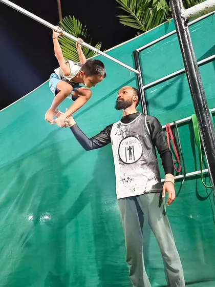A coach providing one-on-one support to a young athlete, helping him build grip strength and confidence on the bar.