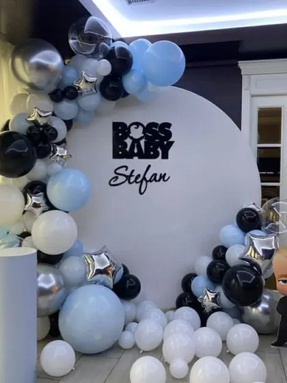 A fun and stylish Boss Baby theme for a little one's birthday. This setup features a clean white circular backdrop with the Boss Baby logo, a character cutout, and a balloon garland in blue, black, and silver.