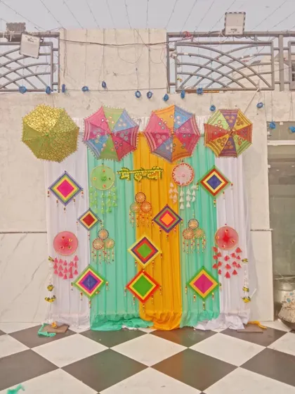 A full view of a Mehendi backdrop against a checkered floor, combining mint green, yellow, and white drapes with various hanging props for a festive look.