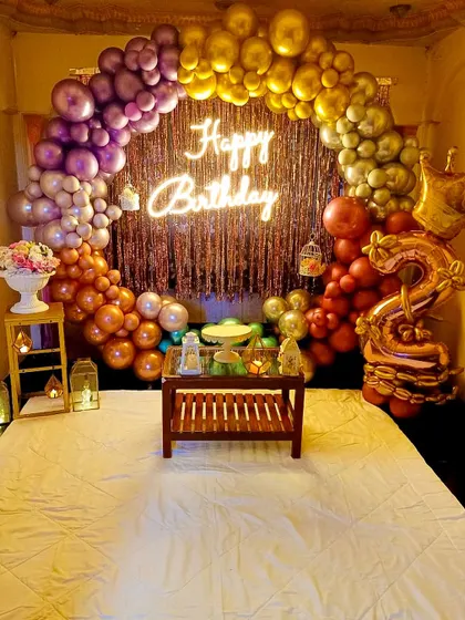 I can even turn a bedroom into a party zone for a special surprise. This setup features a vibrant rainbow-colored balloon arch over the bed, a shiny fringe curtain, and a "Happy Birthday" neon sign.