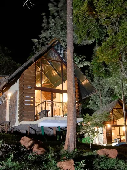 The same cottage illuminated at night, creating a warm and inviting beacon in the forest. The design provides a sense of safety and comfort while maintaining a close connection to the wild.