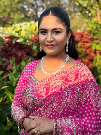 A portrait of the daughter, Supriya, looking radiant in a pink bandhani saree. Her makeup is fresh and glowing, with a sleek ponytail and diamond jewellery for a modern touch.