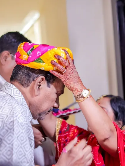 A close-up of a traditional ritual, where a woman places a colorful turban on a man's head as a sign of respect.