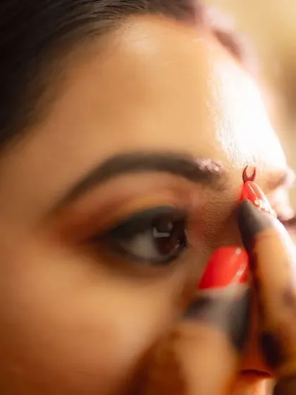An intimate close-up of a bride getting her bindi applied. This macro shot focuses on the small, traditional detail, symbolizing a key moment in her bridal transformation.